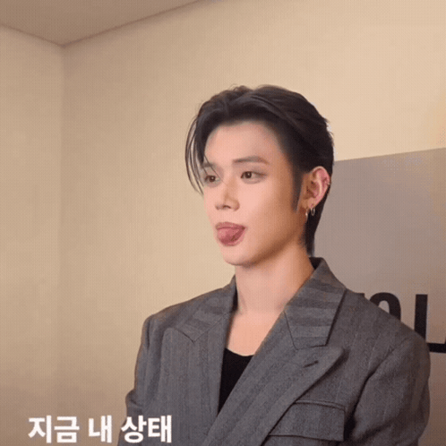 a young man in a suit sticking his tongue out with korean writing behind him