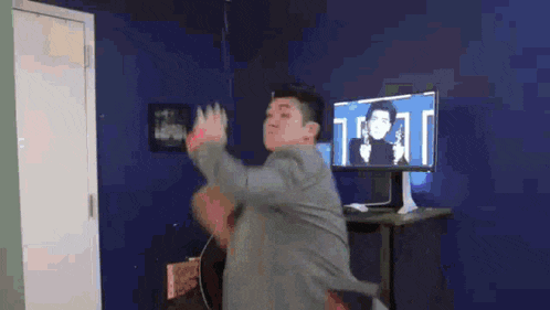a man in a suit is dancing in a room in front of a computer screen .