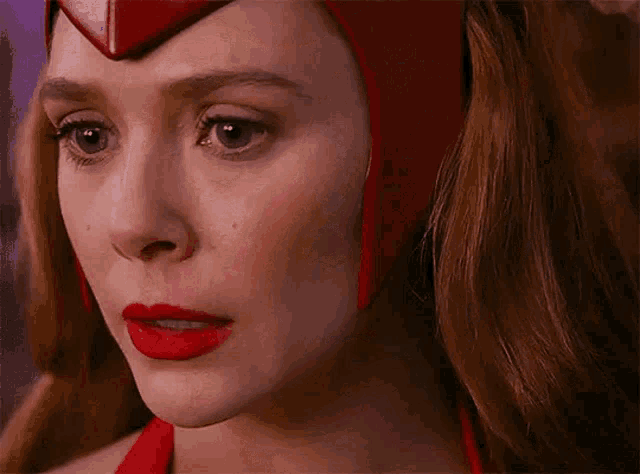 a close up of a woman 's face with red lipstick and red eyes wearing a red helmet .