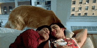 two men laying on a bed with a dog