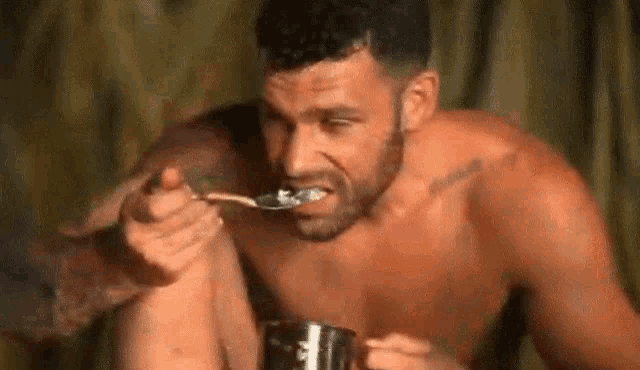 a shirtless man is eating a spoonful of food from a cup .