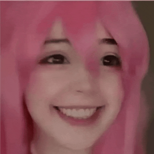 a close up of a girl wearing a pink wig smiling .