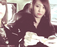 two women are sitting in a car and one is holding a sandwich