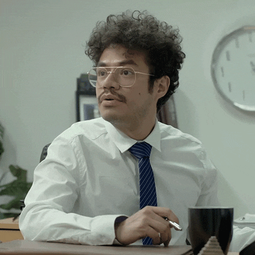 a man with glasses and a mustache sits at a desk with a cup of coffee