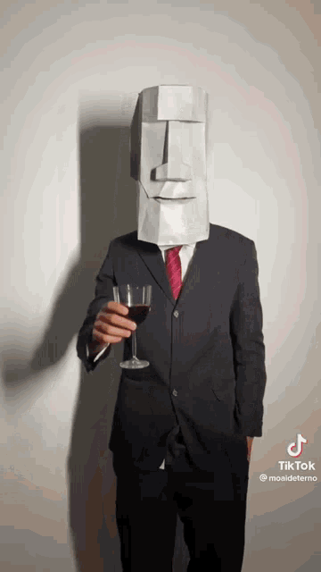 a man in a suit and tie with a statue on his head holding a glass of wine