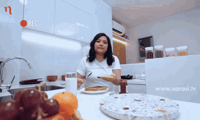 a woman in a white t-shirt is eating in a kitchen