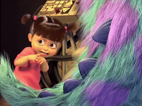 a little girl in a pink shirt is sitting next to a purple and green monster