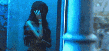 a woman is standing in front of a blue light and covering her face with her hands .