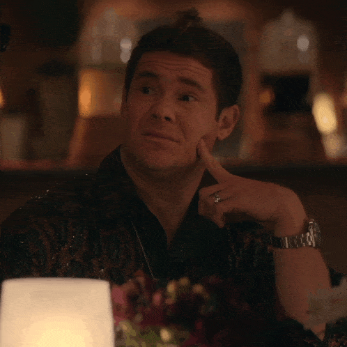 a man with a ring on his finger is sitting at a table with his hand on his chin