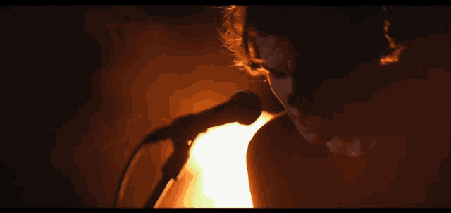 a person singing into a microphone with a fire in the background