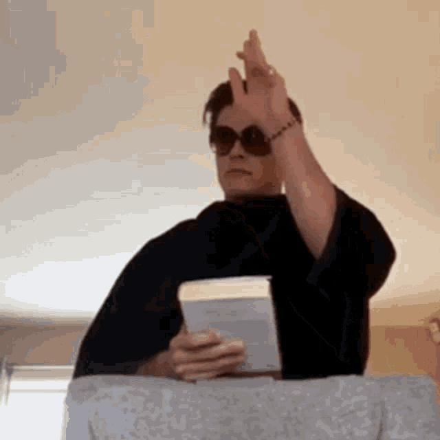 a man wearing sunglasses is holding a book and giving the middle finger .