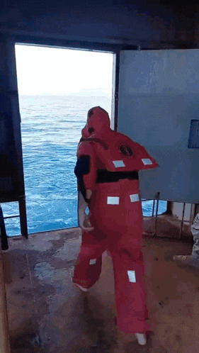 a man in a red life jacket walks out of a doorway into the ocean