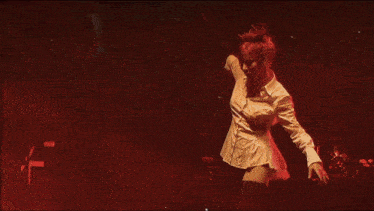 a woman in a white dress is dancing in a dark room with her arms outstretched .