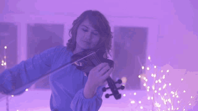 a woman is playing a violin in a room with purple lights behind her