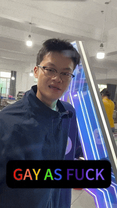 a man wearing glasses stands in front of a sign that reads gay as fuck