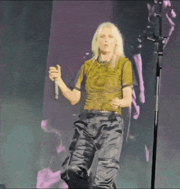 a woman in a yellow top and black pants is singing into a microphone