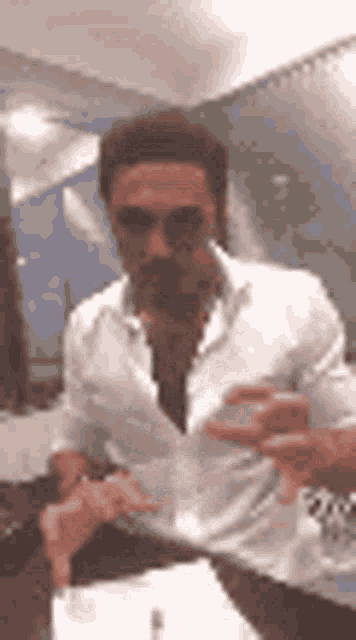 a man in a white shirt is sitting at a table drinking a glass of water .