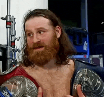 a man with a beard and long hair is holding a wrestling championship belt .