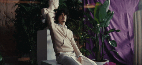 a man is sitting on a pedestal next to a plant and a statue