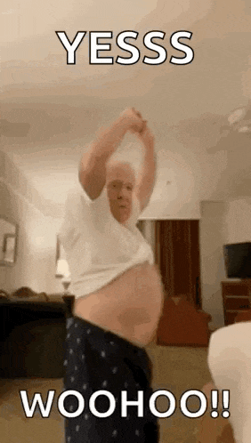 an older man is standing in a living room with his shirt off and his belly visible .
