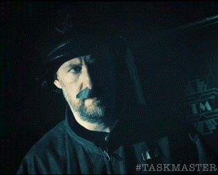 a man is eating a banana in a dark room with the hashtag #taskmaster on the bottom