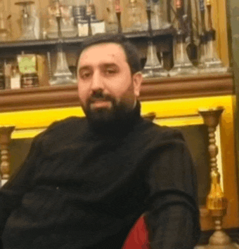 a man with a beard is sitting in a chair in front of a shelf full of hookahs