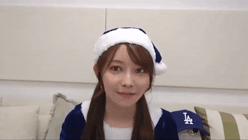 a young woman wearing a santa hat and a la hat is sitting on a couch .