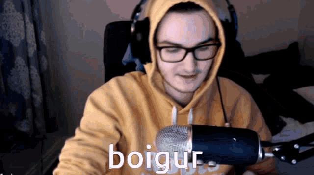 a man wearing headphones and a yellow hoodie stands in front of a microphone that says boigur on it