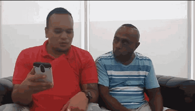 a man in a red shirt is looking at a cell phone