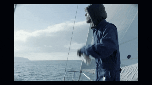 a man in a blue jacket is standing on a boat in the water