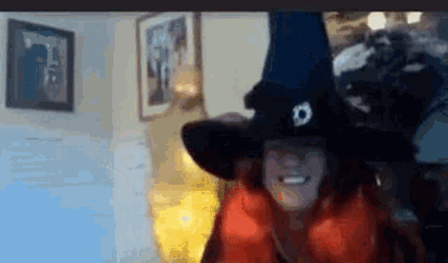 a woman is wearing a witch hat and smiling while sitting in a living room .