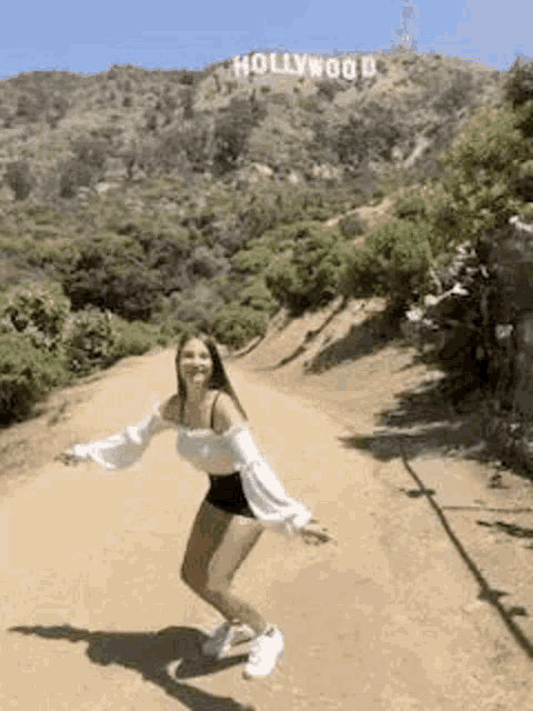 a young woman is standing in front of the hollywood sign .