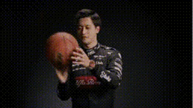 a man in a race car jacket is holding a basketball in his hand .