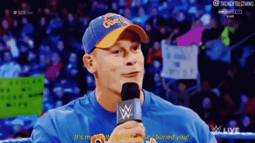 a man is talking into a microphone while wearing a blue shirt and hat .