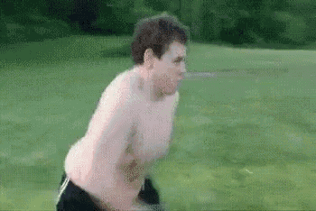 a shirtless man is running in a field with a sword in his hand .