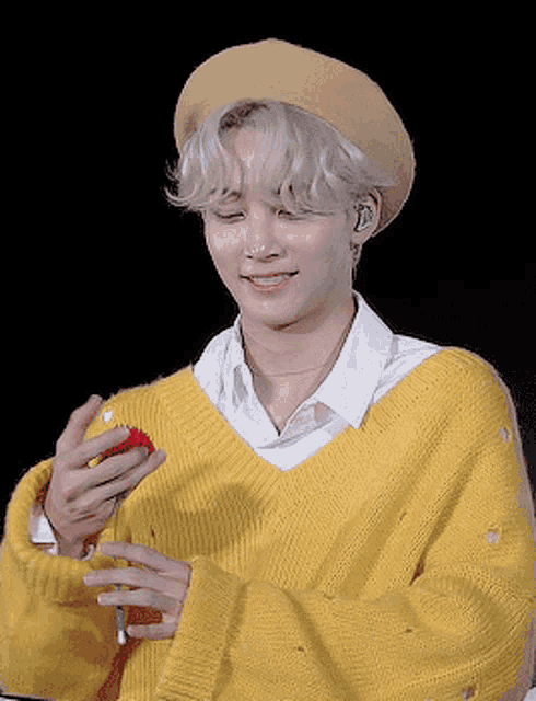 a young man wearing a yellow sweater and a yellow hat is holding a red cube in his hand .