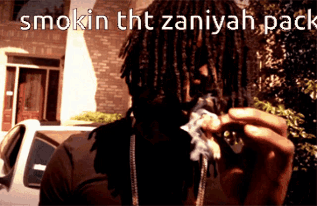 a man with dreadlocks is smoking a cigarette with the words smokin tht zaniyah pack below him