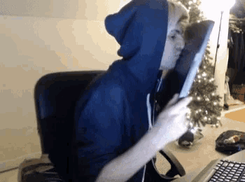 a man wearing a blue hoodie is sitting in front of a laptop
