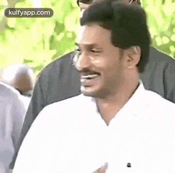 a man in a white shirt is smiling and laughing while standing in a crowd .