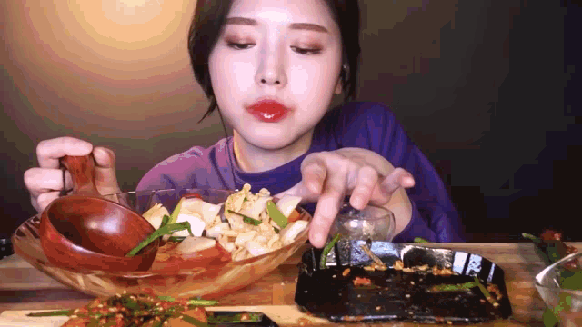 a woman in a purple shirt is eating food from a bowl