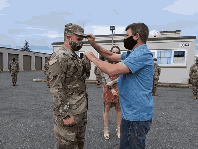 a man in a blue shirt helps a soldier with his hat