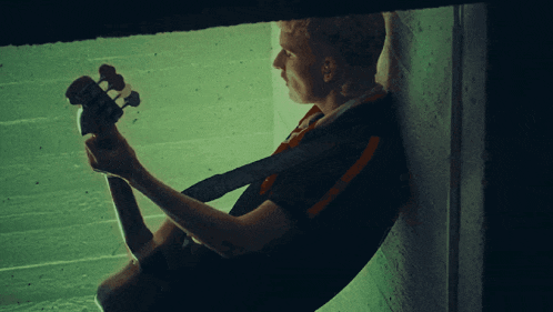 a man leaning against a wall holding a guitar