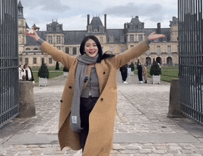a woman in a coat and scarf is standing in front of a castle