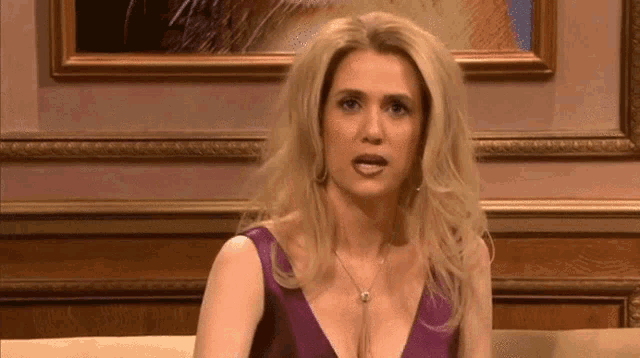 a blonde woman in a purple dress is sitting on a couch .