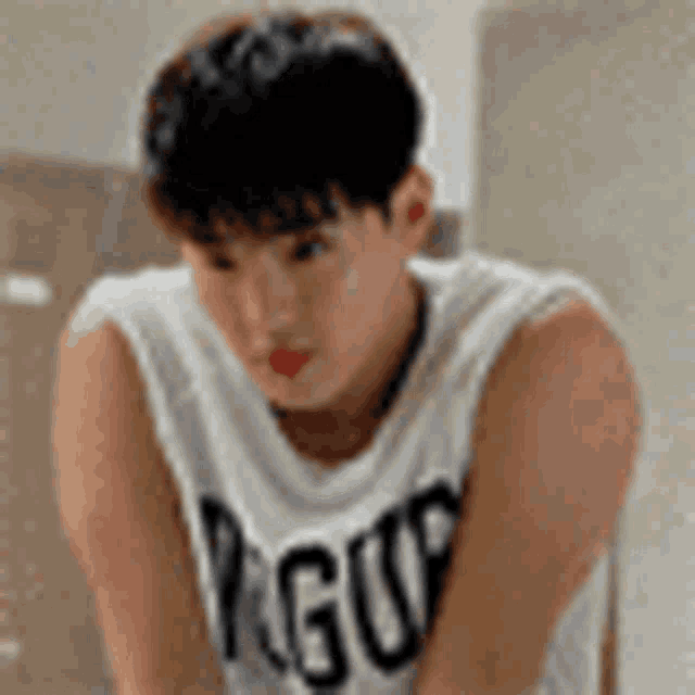 a young man wearing a white tank top is sitting on a chair and looking down .