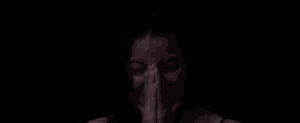 a woman is praying with her hands folded in front of her face in the dark .