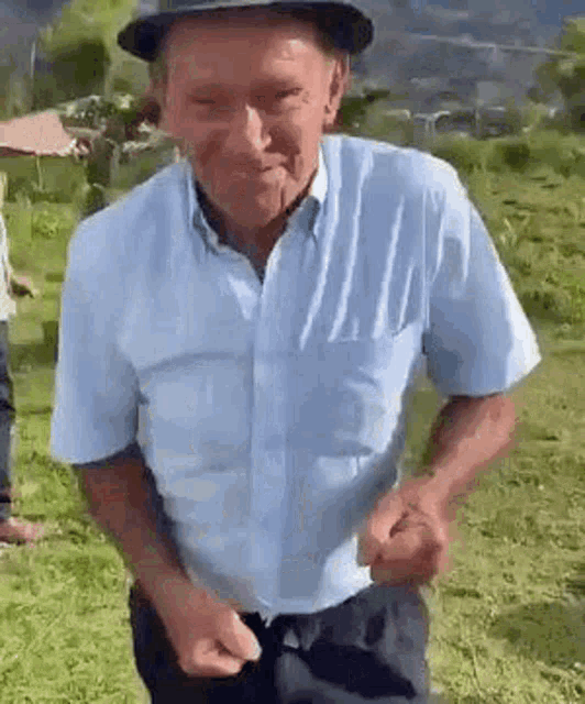 an elderly man wearing a hat and a blue shirt is dancing in a grassy field .