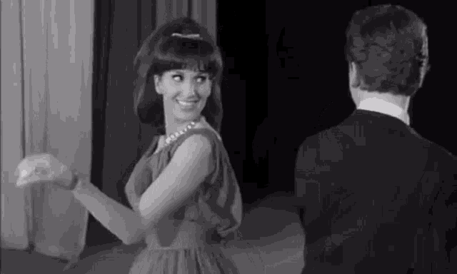 a black and white photo of a woman in a dress dancing with a man in a tuxedo .