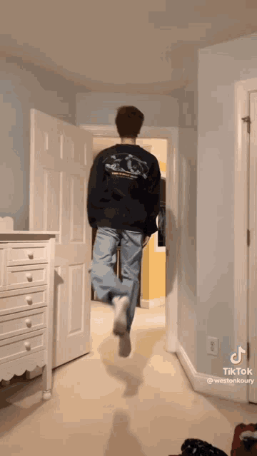 a man in a black sweatshirt is jumping in the air in a hallway