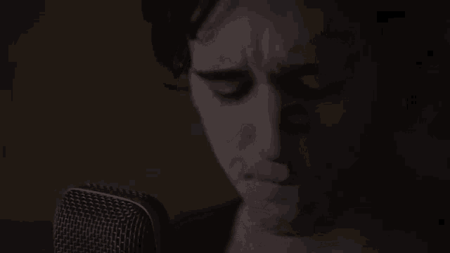 a close up of a man singing into a microphone in a dark room .